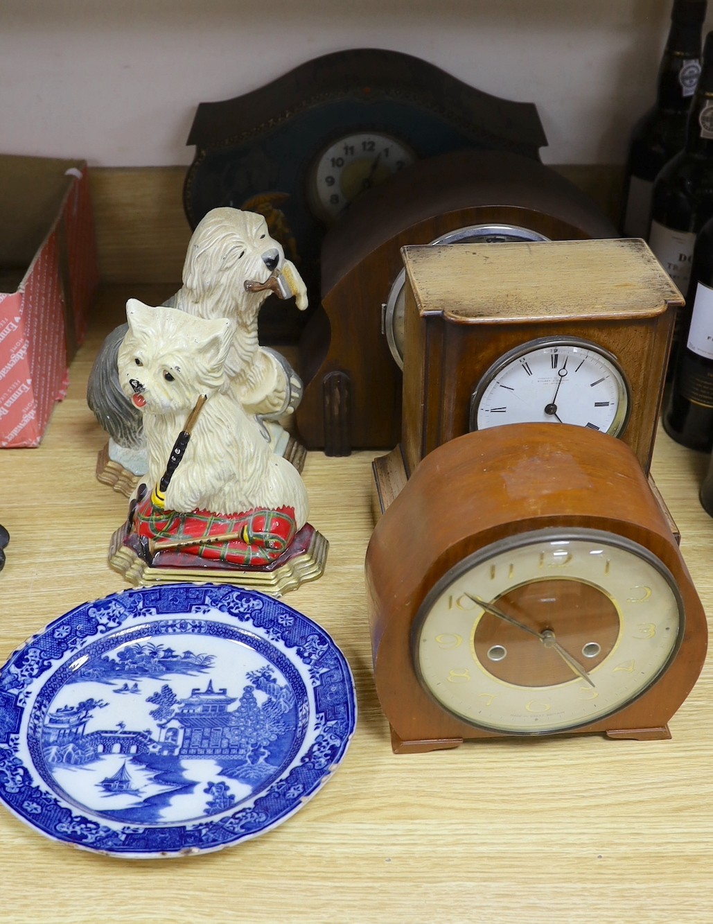 A tin mantel clock and 3 wooden clocks, 2 dog door stops and a blue and white plate.